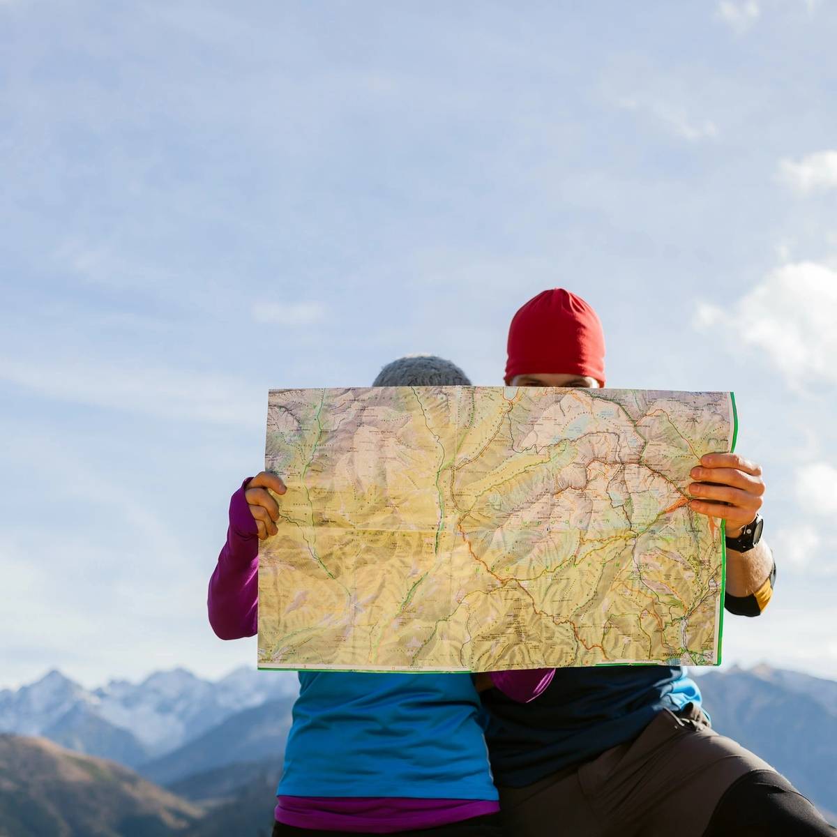 A couple stands outdoors, holding a map while surrounded by mountains and clear skies.