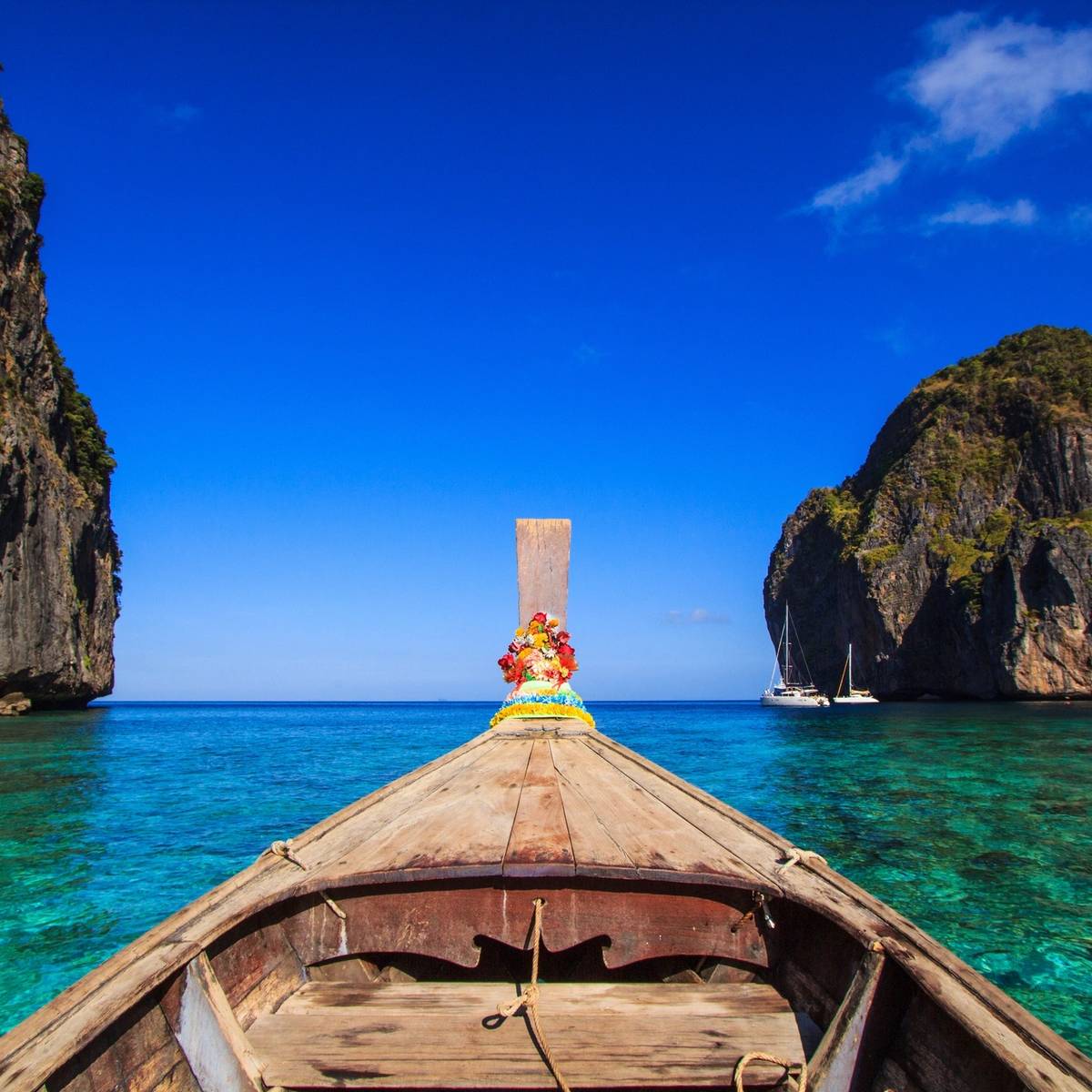 A scenic view from the bow of a boat, turquoise waters surrounded by rocky cliffs under a blue sky.